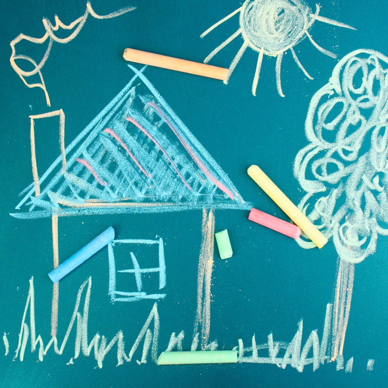 Bild auf einer Tafel, mit Kreide wurde ein Haus mit Kamin, Baum, eine Sonne gemalt. 