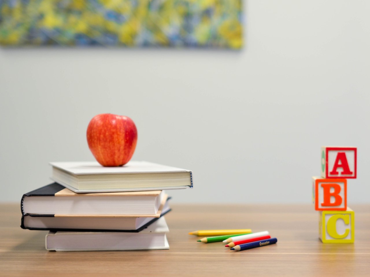 Apfel, Bücher, Farbstifte und ABC-Klötze auf einem Tisch